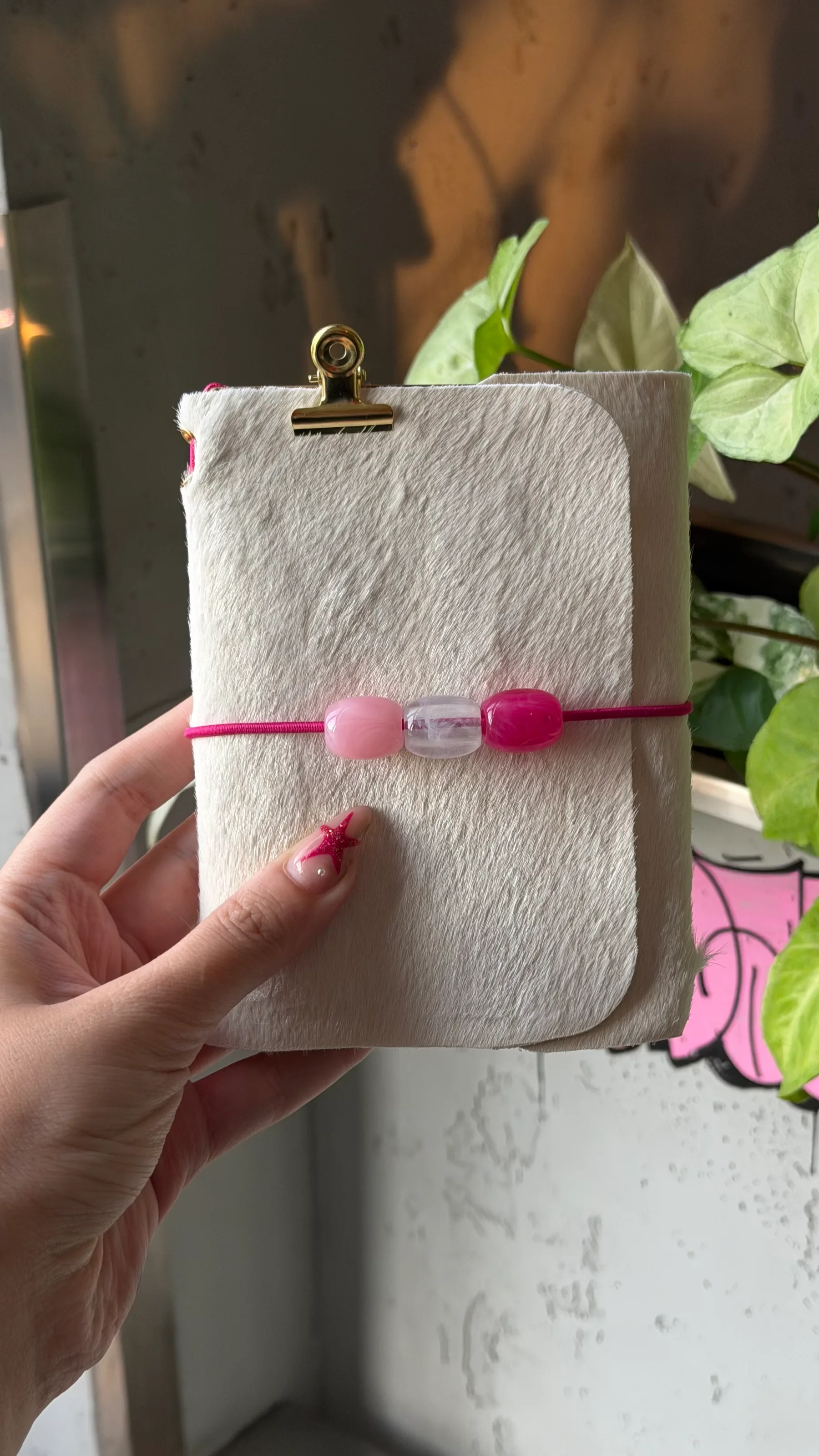 Small cream journal with a pink cord and three pink-and-clear decorative beads.